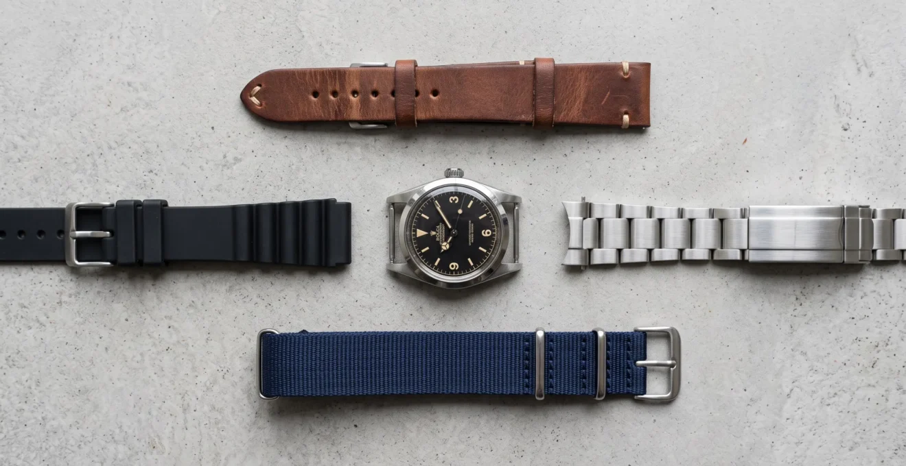Vue du dessus montrant une montre entourée de différents types de bracelets : cuir, acier, NATO et caoutchouc